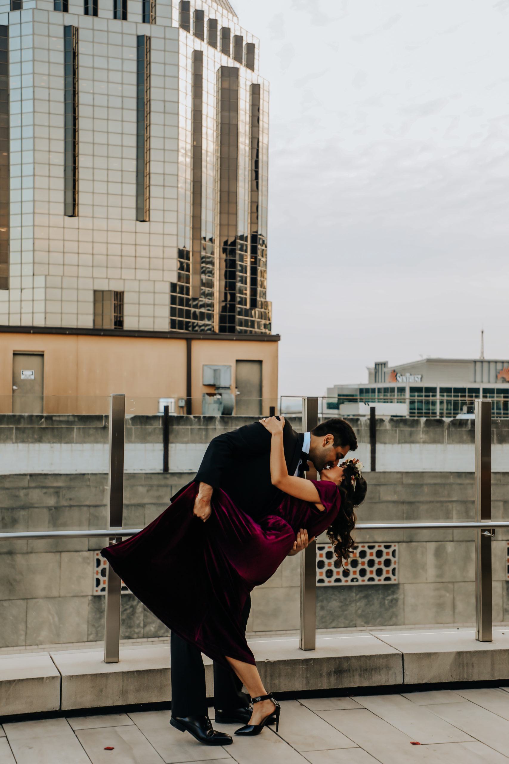A couple standing on a rooftop in downtown Nashville, they are in the middle of a dip and are kissing.