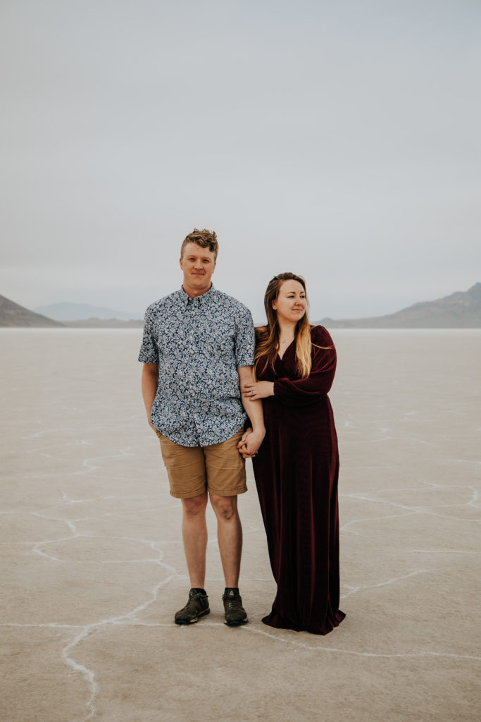 A couple standing in the salt flats they are holding hands and the woman has her hand on her partners arm. They are looking in opposite directions