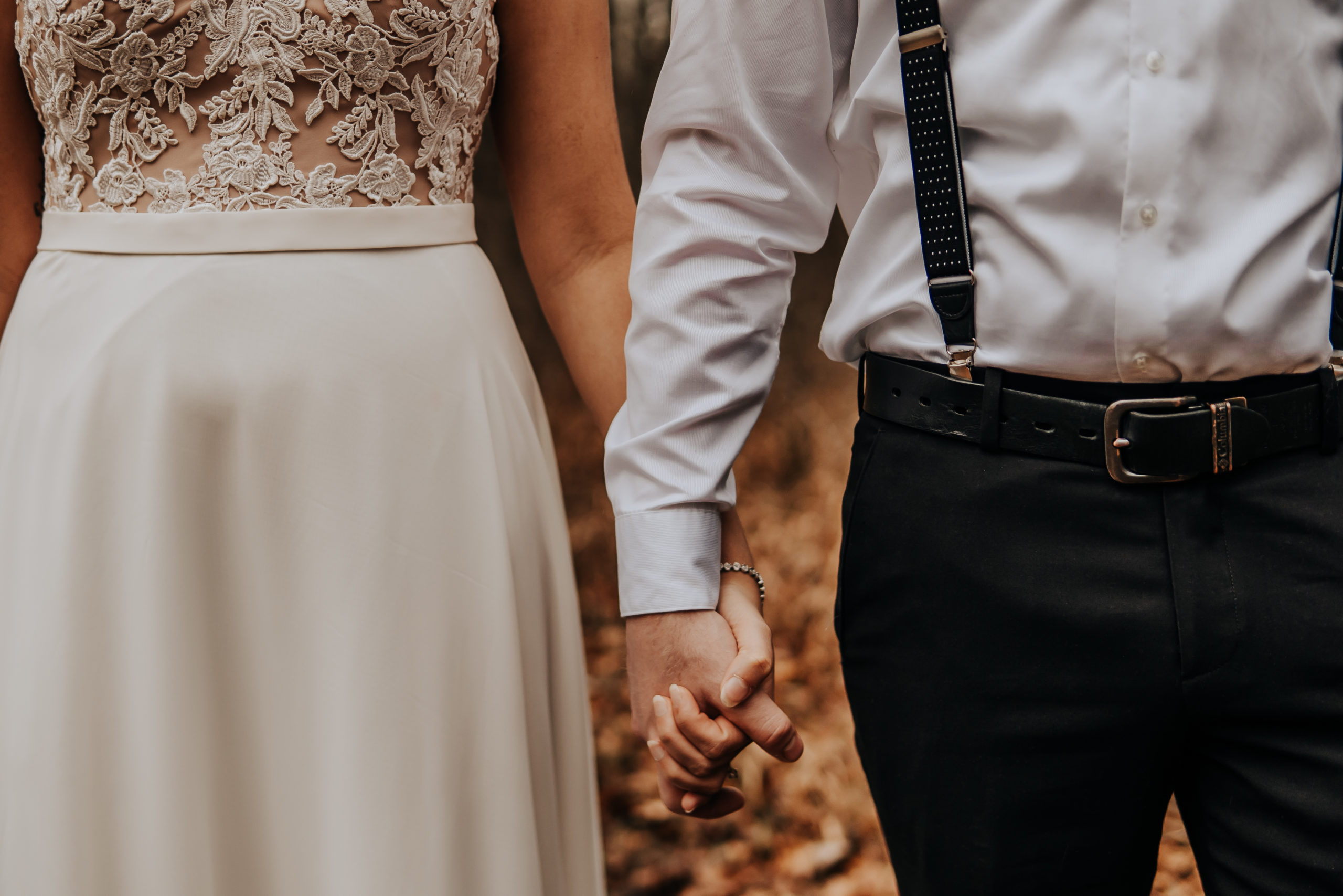 A close up image of a couple holding hands, you can't see their faces. But you can tell they are facing the camera and are wearing their wedding attire.