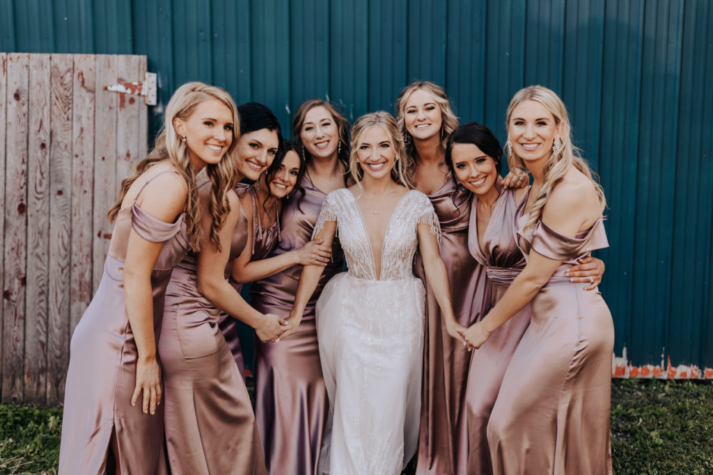 Minnesota wedding party photograph of a bride surrounded by bridesmaids they are all smiling at the camera and the bride has her hands reached out to hold her bridesmaids hands.