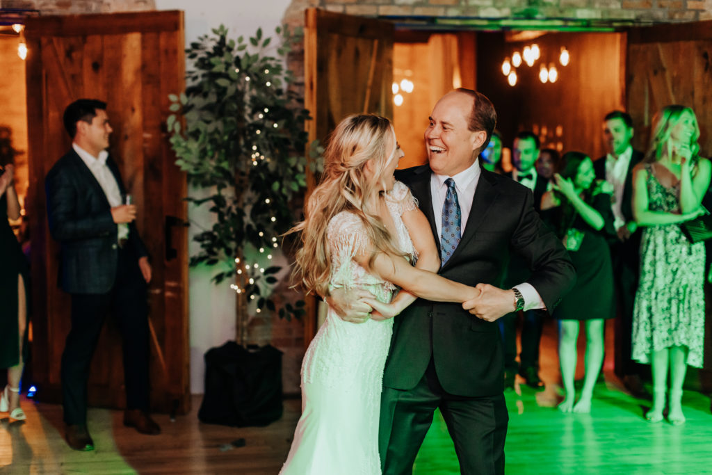 Minnesota wedding reception image of a bride dancing with her father in law. Both are holding hands, and leaning forward while smiling at each other. 
