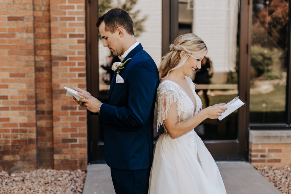 Minnesota wedding photo of a bride and groom standing back to back They are smiling and reading letters. 