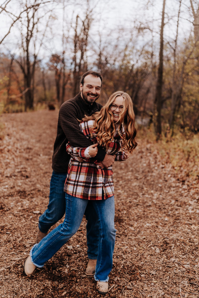 A straight couple's engagement photo. They are laughing and looking at the camera as the male holds onto his fiance. Minnesota engagement photographer. 