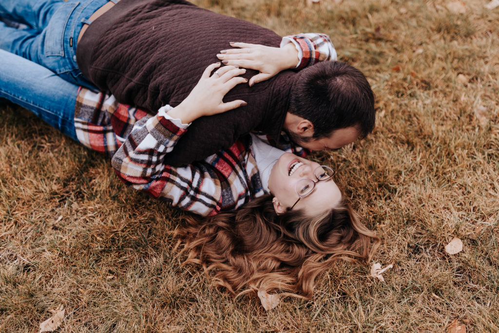 Romantic overhead shot of a couple laughing while lying in the grass, wrapped up in each other on a chilly fall day.