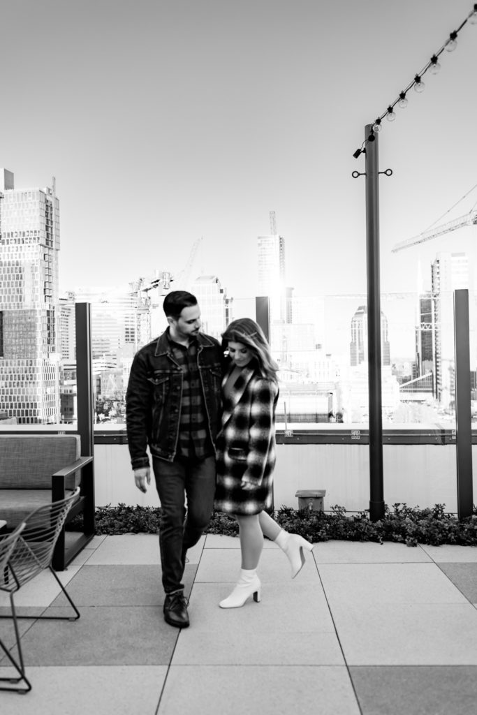A black and white image of a couple holding hands and walking towards the camera. One of them is looking down and the other is looking at their partner. Nashville rooftop engagement session