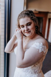Bride standing in front of a window putting her earrings on. She has a faint smile. Nashville wedding photographer, Nashville country club wedding