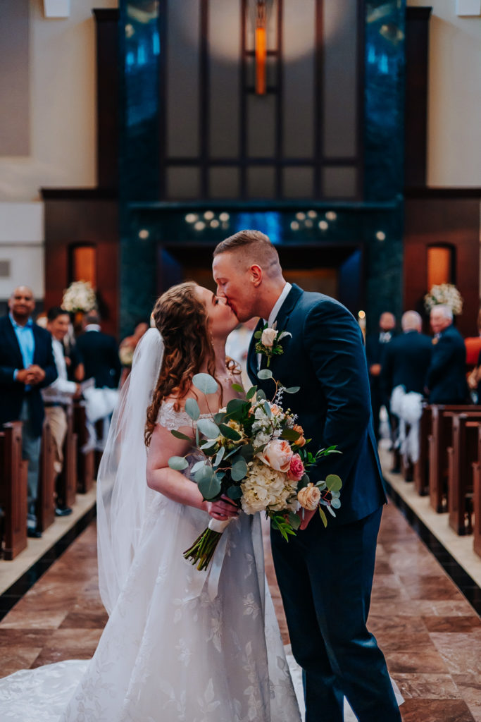 Wedding photo of a couple kissing in the aisle of a catholic church. Nashville wedding photographer. Nashville country club wedding. 