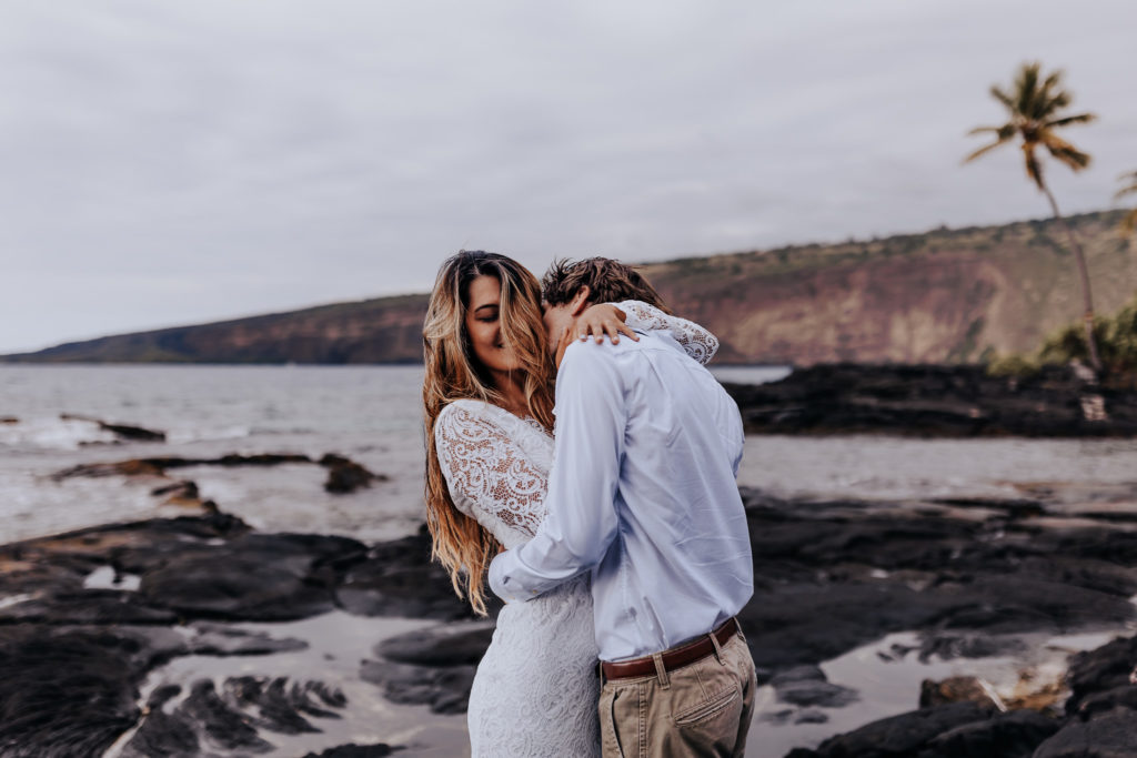 a couple holding each other. the groom is kissing the brides neck while her eyes are closed and she's smiling. her hair is in her face. big island beach elopement
