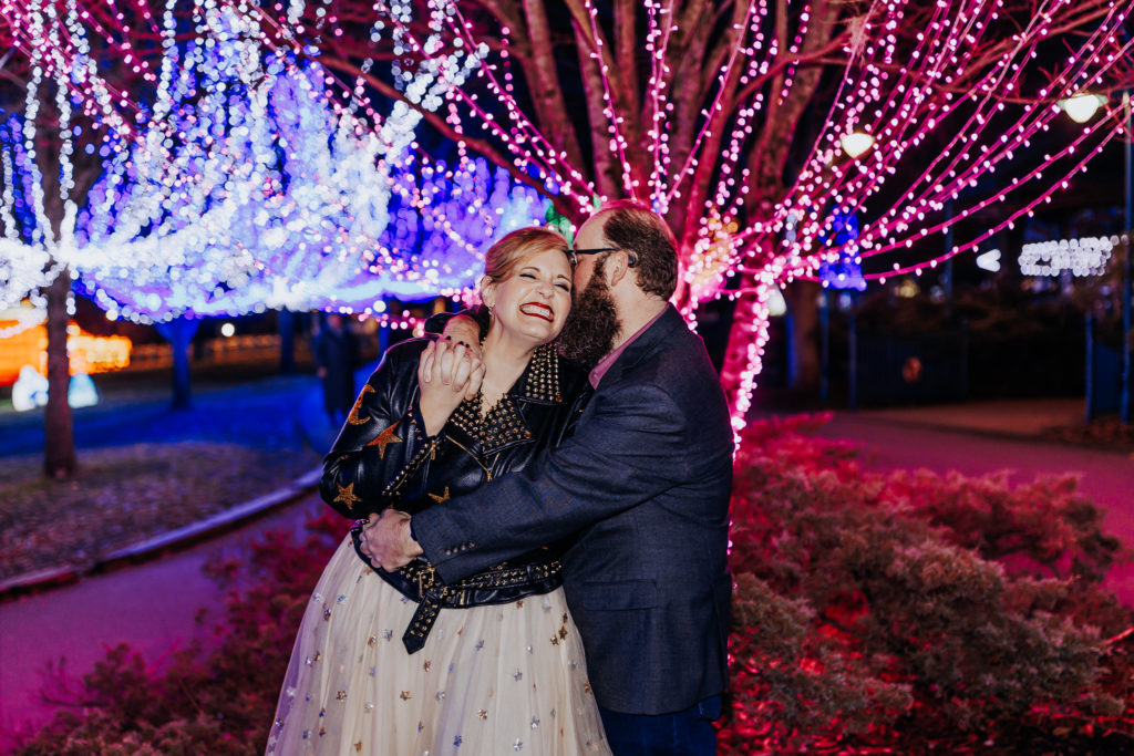 A couple holding hands at night surrounded by lights. Nashville Zoo Elopement