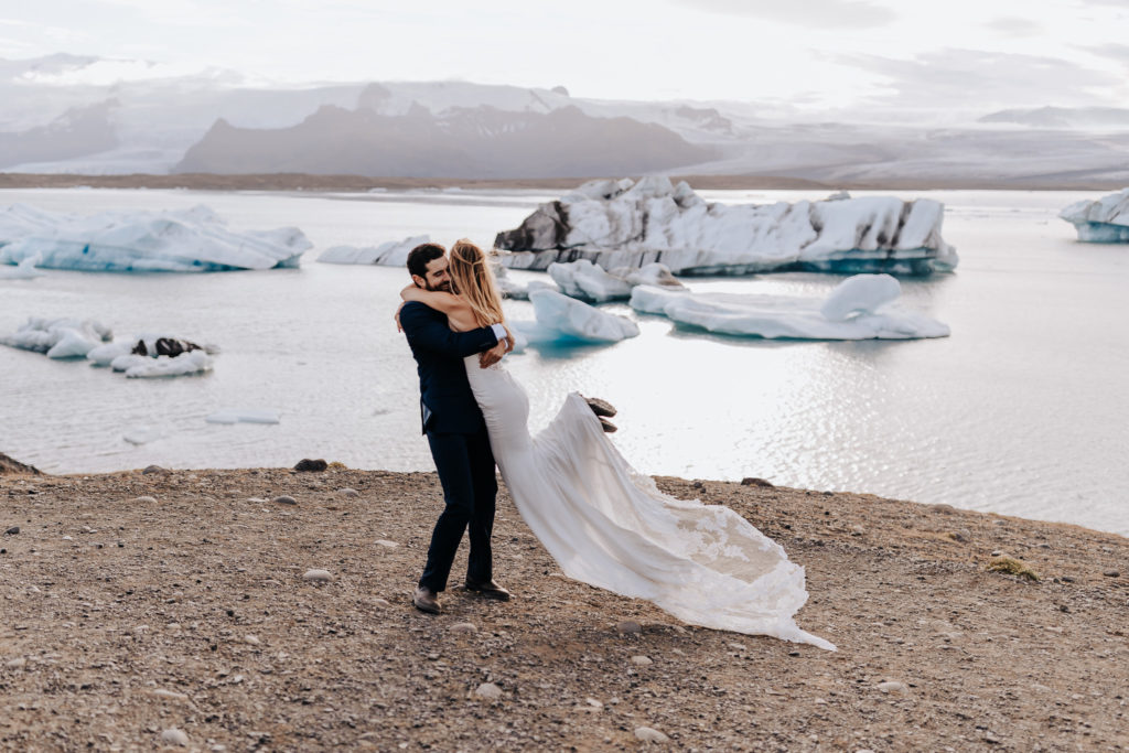 Iceland elopement photographer captures groom lifting bride and spinning her on cold beach in Iceland