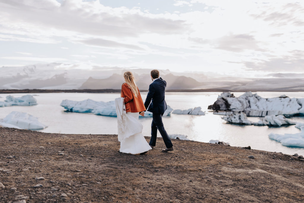Iceland elopement photographer captures couple walking alongside beach in wedding attire
