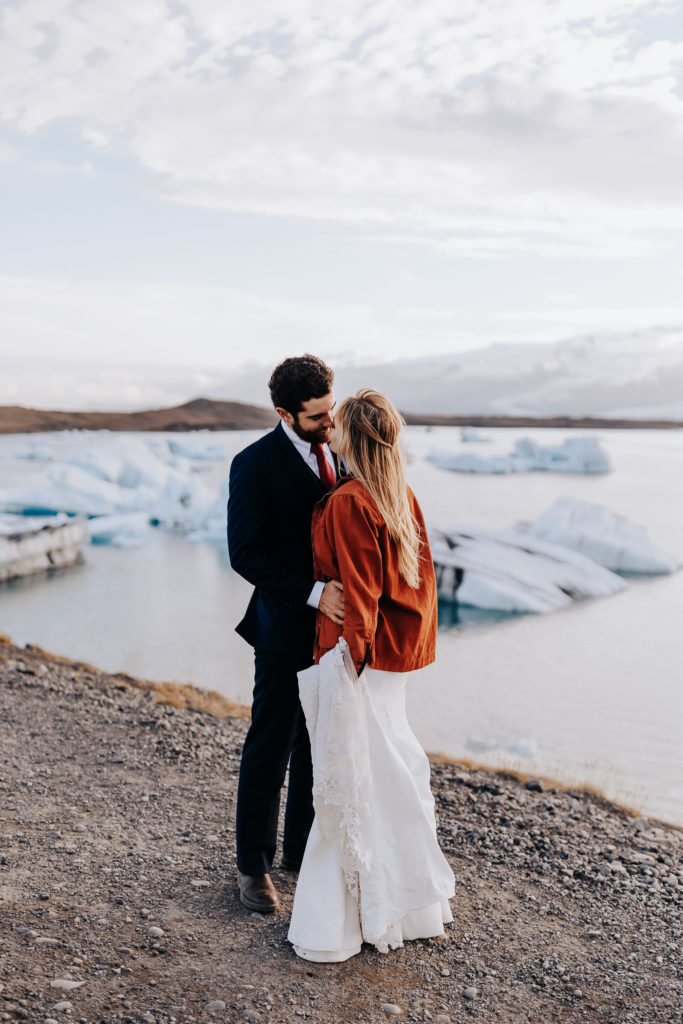 Destination Wedding Photographer captures bride and groom kissing on beach in Iceland whild bride wears wedding dress and jacket