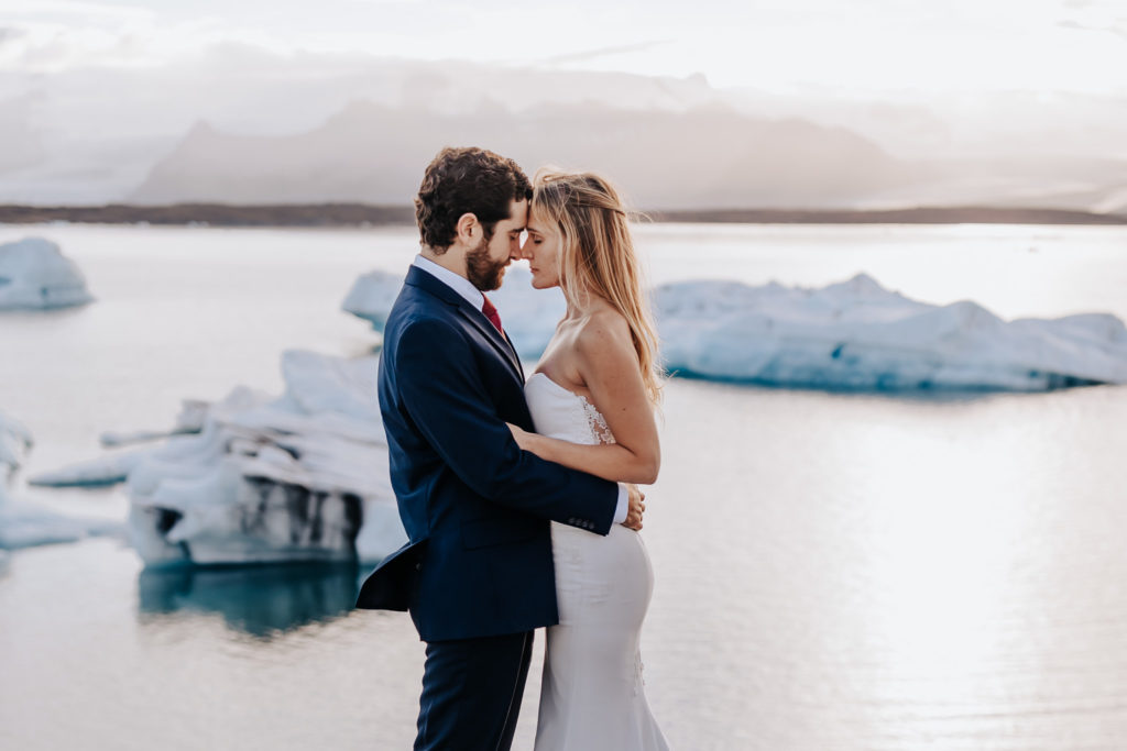 A couple touching foreheads together with their arms wrapped around each other and their eyes closed. Iceland Ice Lagoon Elopement