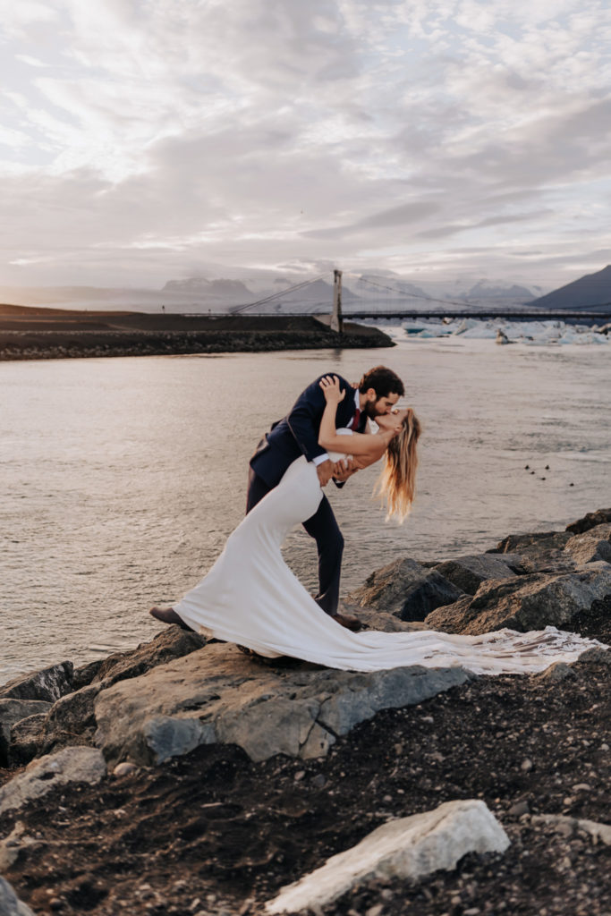 Destination Wedding Photographer captures bride and groom dip kiss on black sand beach in Iceland