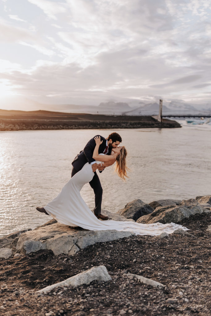 Destination elopement photographer captures groom dip kissing bride on beach after Iceland elopement