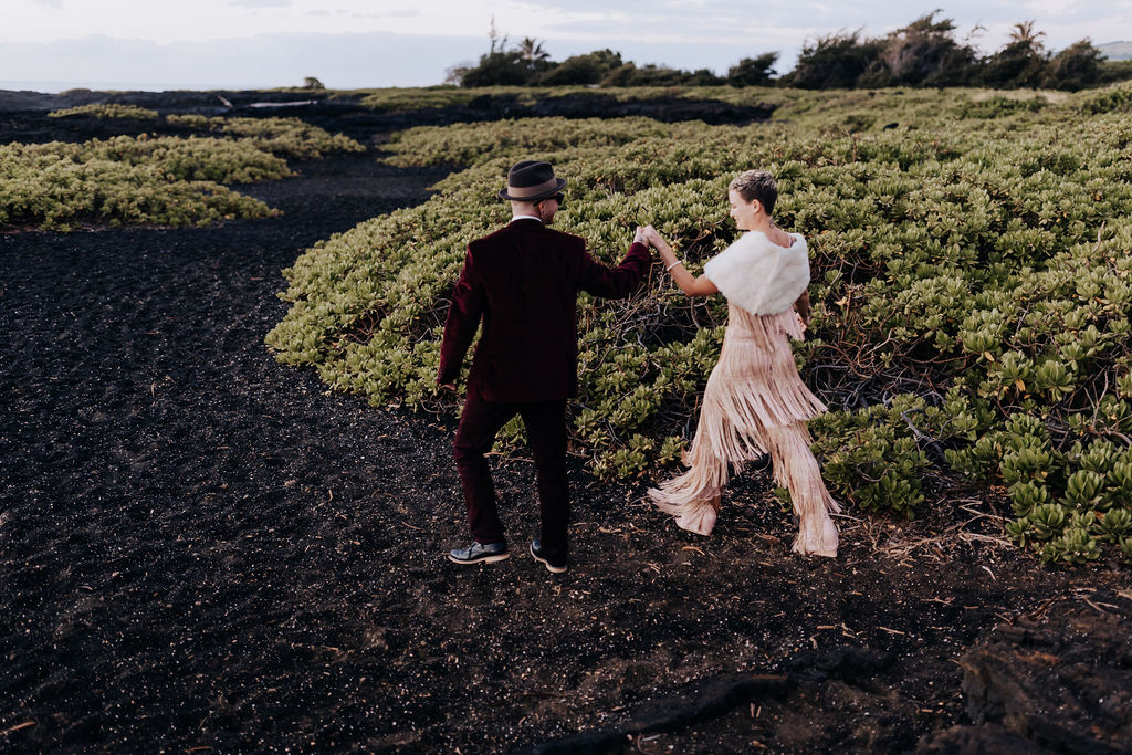 Destination elopement photographer captures couple walking along black beach in Hawaii