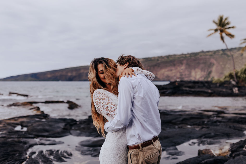 Destination elopement photographer captures bride and groom embracing on beach after eloping in Big Island