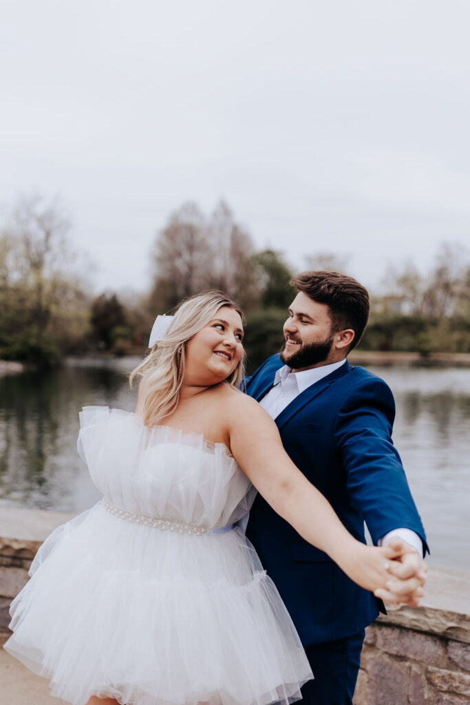 Nashville elopement photographer captures couple holding hands and twirling together alongside water at Centennial Park
