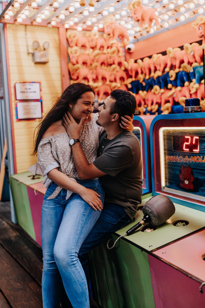 Nashville elopement photographer captures couple sitting on counter of carnival games during unique engagement session