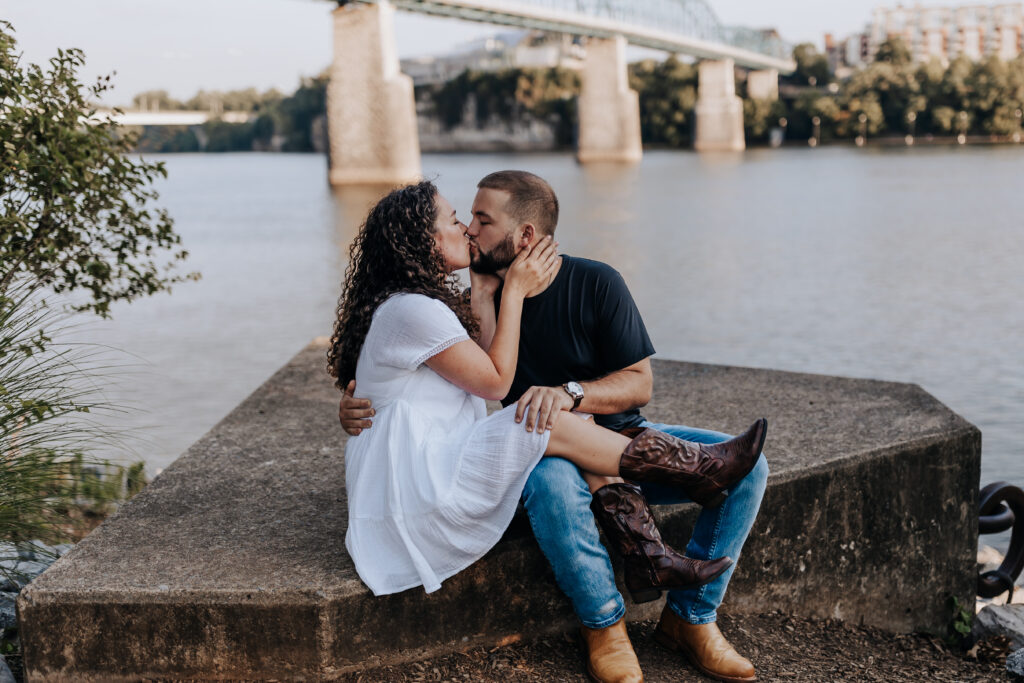 Nashville elopement photographer captures couple sitting together and kissing while wearing summer engagement outfit