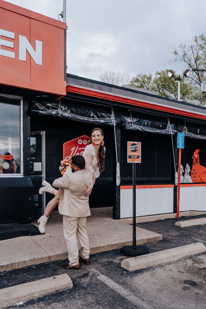 Nashville elopement photographer captures couple outside Hattie B's while groom lifts bride