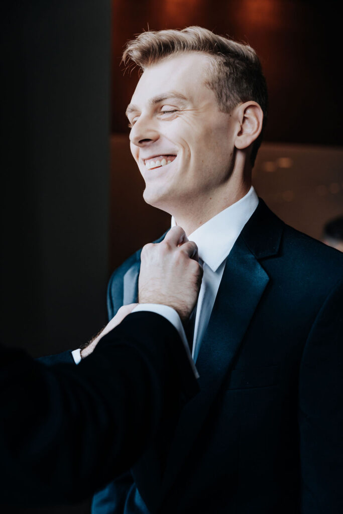 Nashville elopement photographer captures someone helping groom adjust tie before wedding ceremony
