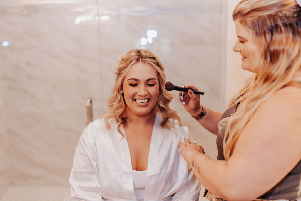 Nashville elopement photographer captures bride smiling while getting makeup on before Asheville cabin wedding