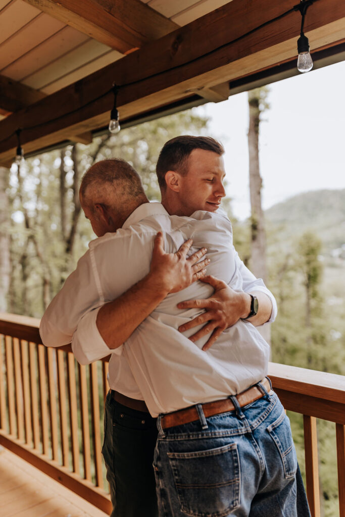 Nashville elopement photographer captures groom hugging groomsman on Asheville cabin wedding day