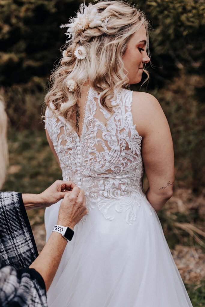 Nashville elopement photographer captures bride getting buttoned into wedding dress before Asheville Cabin wedding