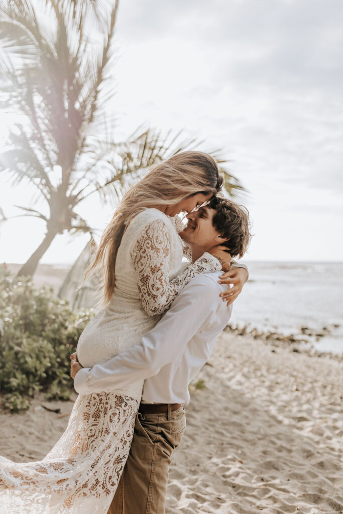 Big Island elopement photographer captures man lifting woman and kissing her during outdoor bridal beach portraits