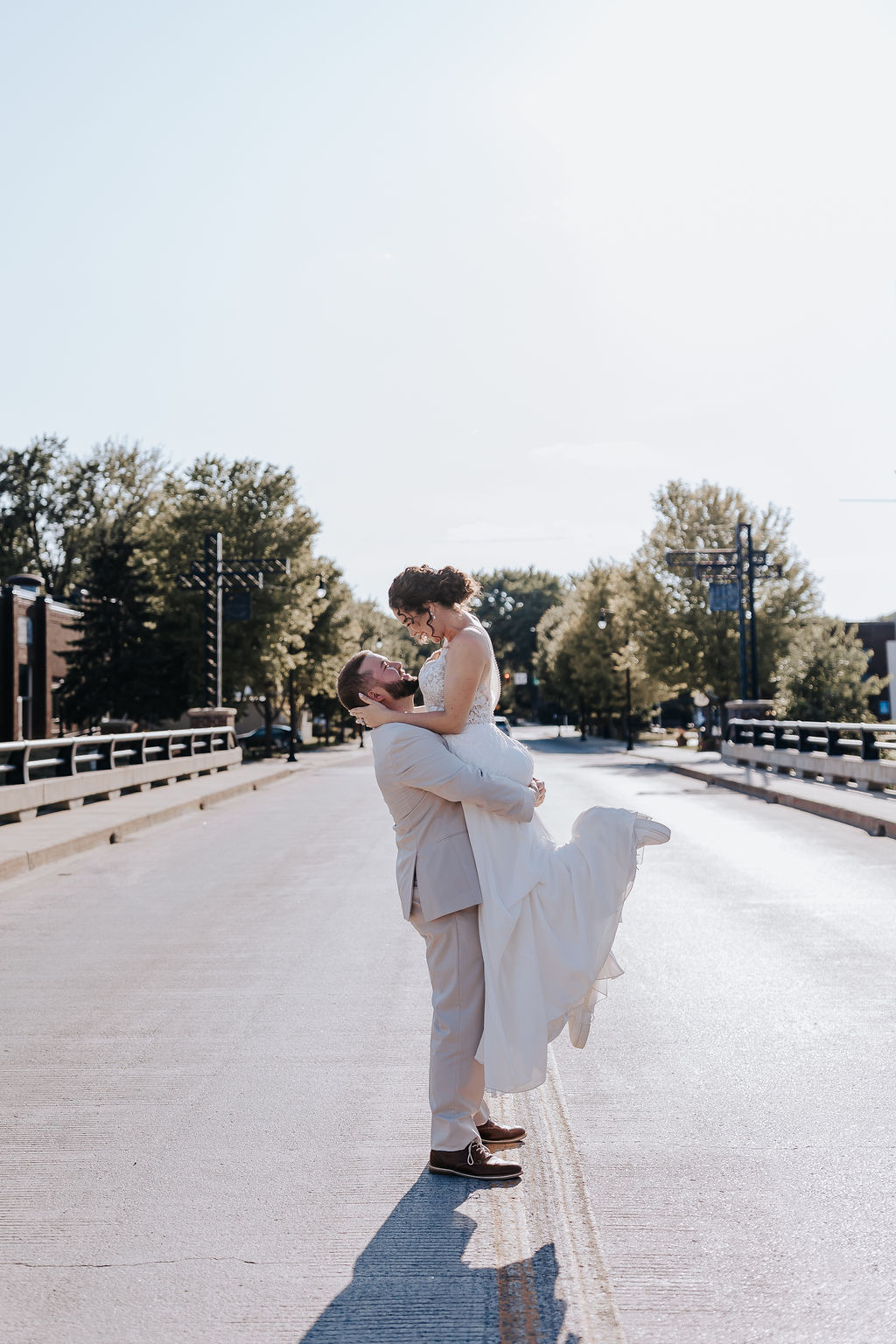 The groom lifts his bride in the center of a quiet street bridge, both smiling under the soft morning light of their Nashville wedding.