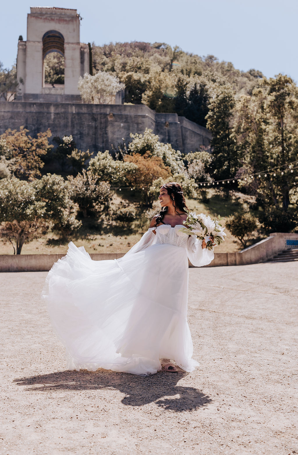 Bride spins in a dreamy off-the-shoulder gown in a sun-drenched courtyard during her Nashville wedding celebration.