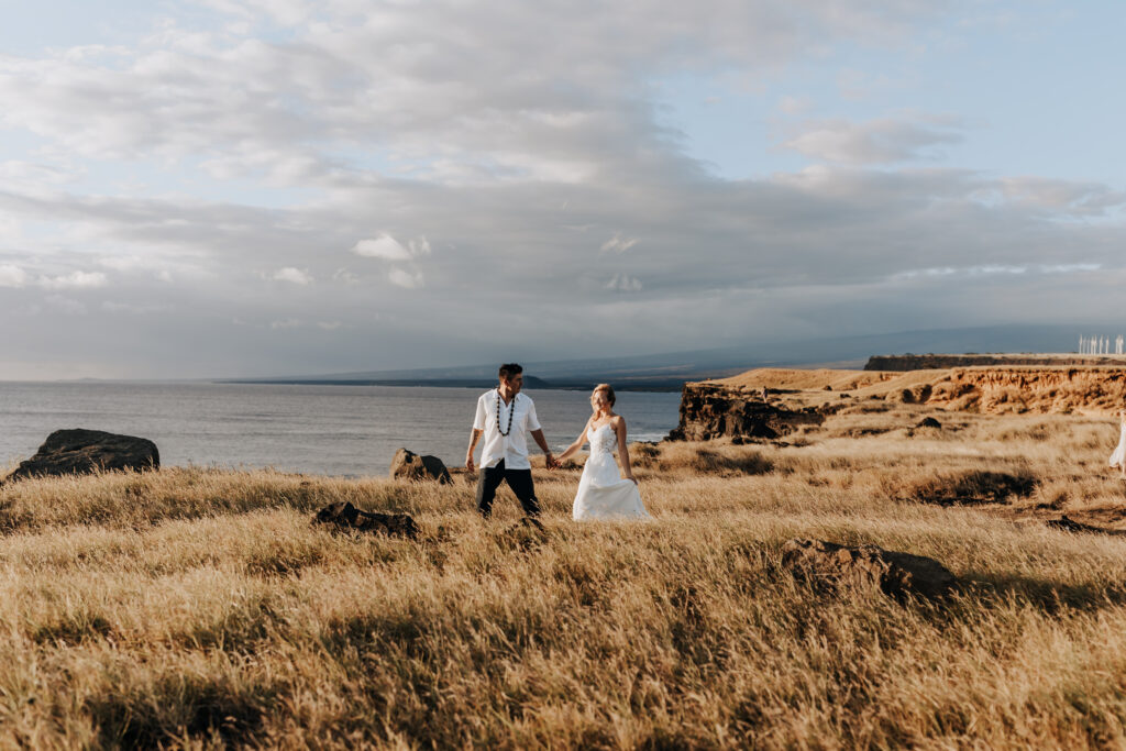 Destination wedding photographer captures bride and groom walking along cliff after Hawaii destination wedding