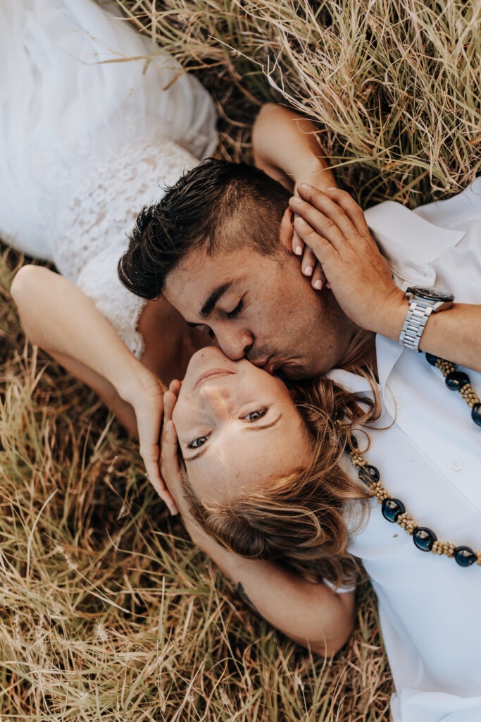 Destination wedding photographer captures bride and groom laying in grass after Hawaii wedding