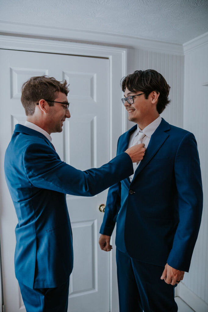 Destination wedding photographer captures groomsmen helping groom get ready for wedding