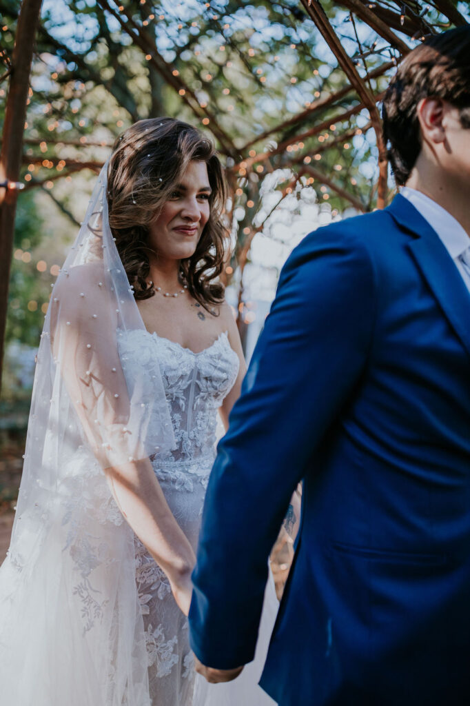 Destination wedding photographer captures bride holding hands with groom from behind before first look
