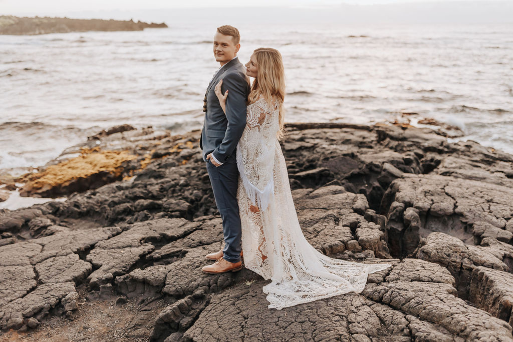 Destination wedding photographer captures bride and groom standing on rock embracing