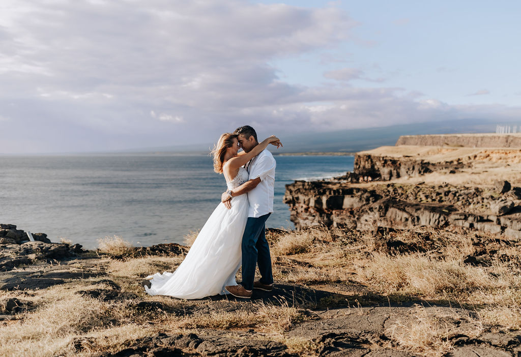 Destination wedding photographer captures bride and groom kissing on cliff after Hawaii beach wedding