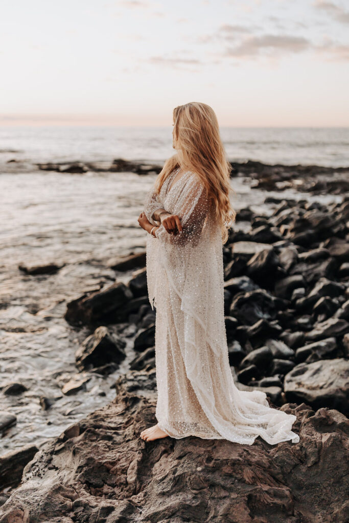 Destination wedding photographer captures bride standing on rock wearing sparkly wedding dress