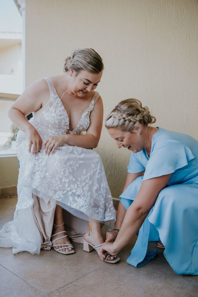 Destination wedding photographer captures bridesmaid helping bride put on shoes