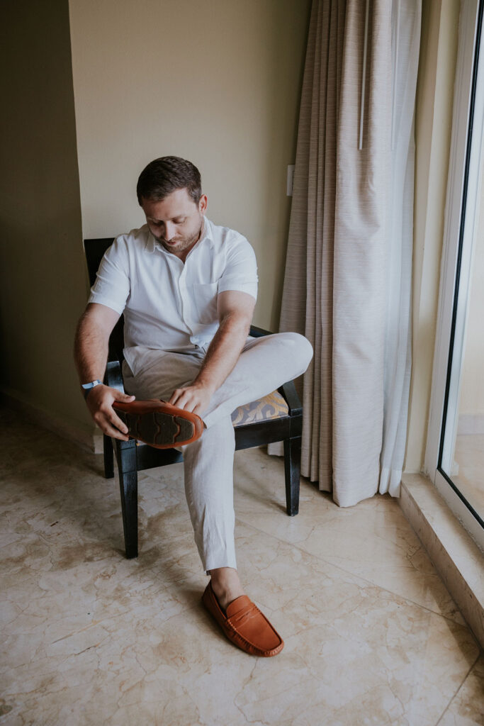 Destination wedding photographer captures groom putting on shoes before Cancun wedding