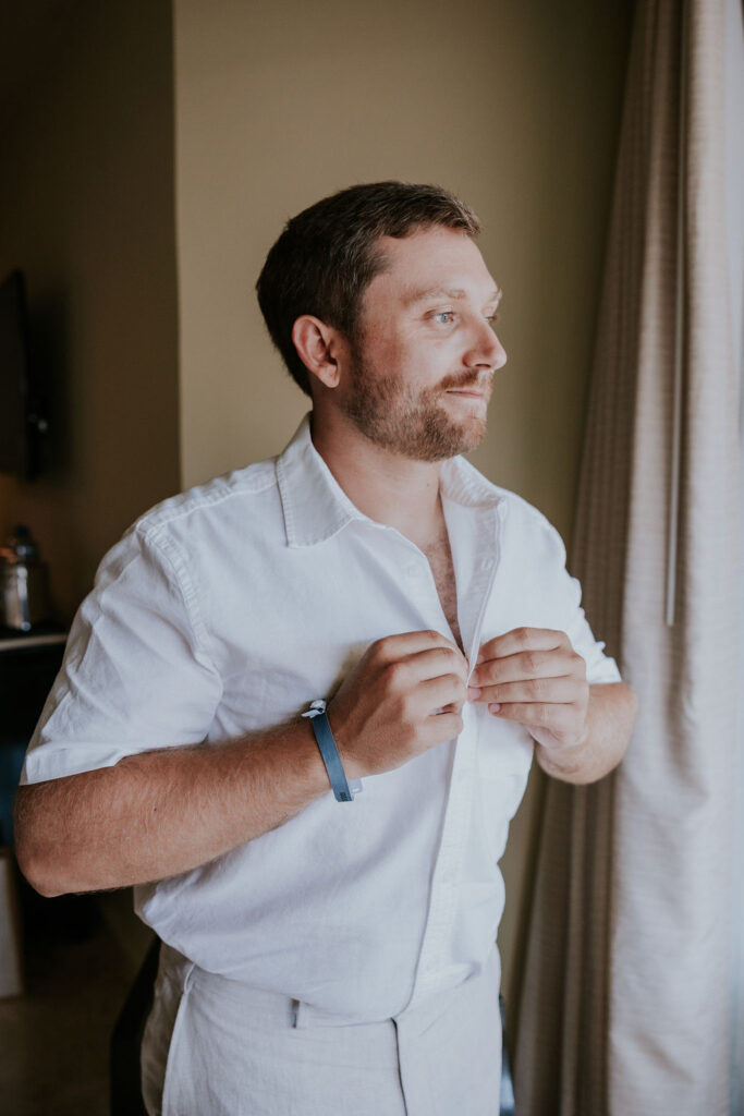 Destination wedding photographer captures groom buttoning shirt