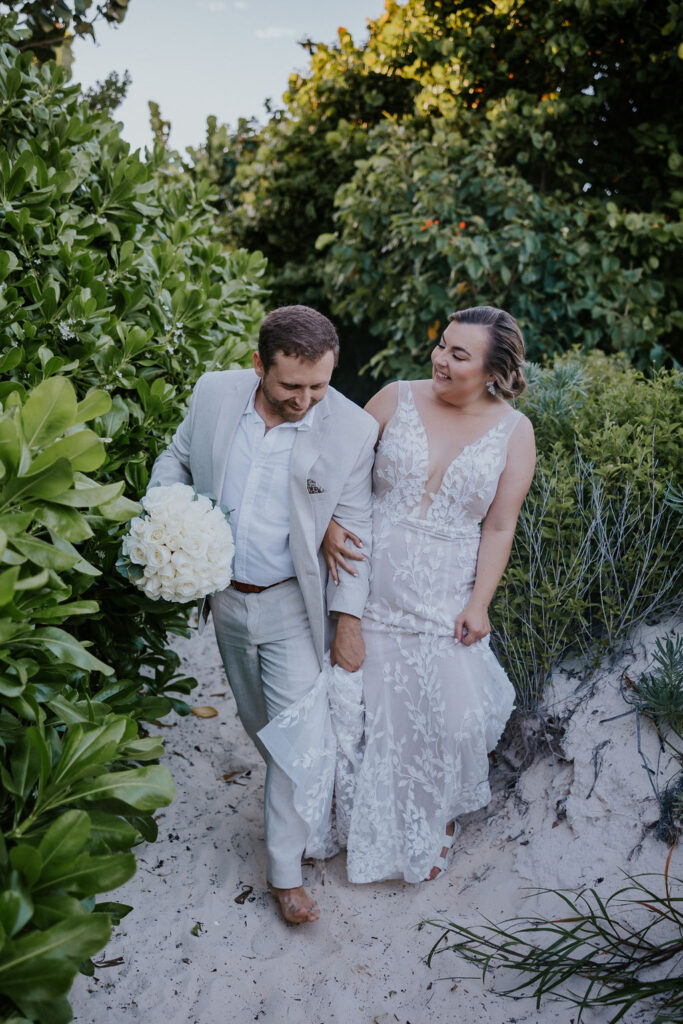 Destination Wedding photographer captures bride and groom walking hand in hand through forest