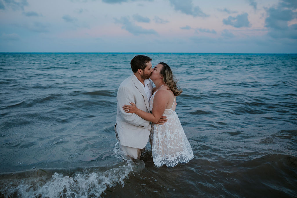 Destination wedding photographer captures bride and groom kissing in ocean