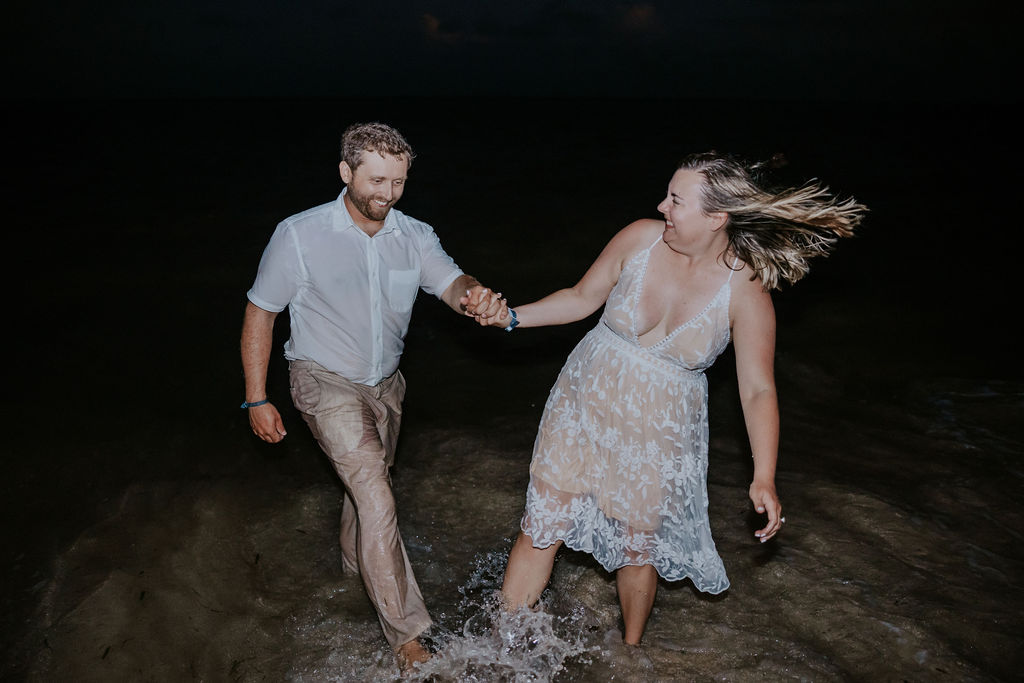 Destination wedding photographer captures bride and groom holding hands in ocean