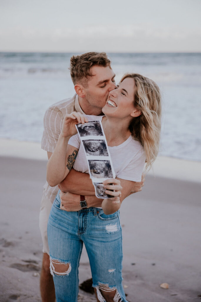 Destination Wedding Photographer captures man kissing woman's cheek while holding up ultrasound pictures