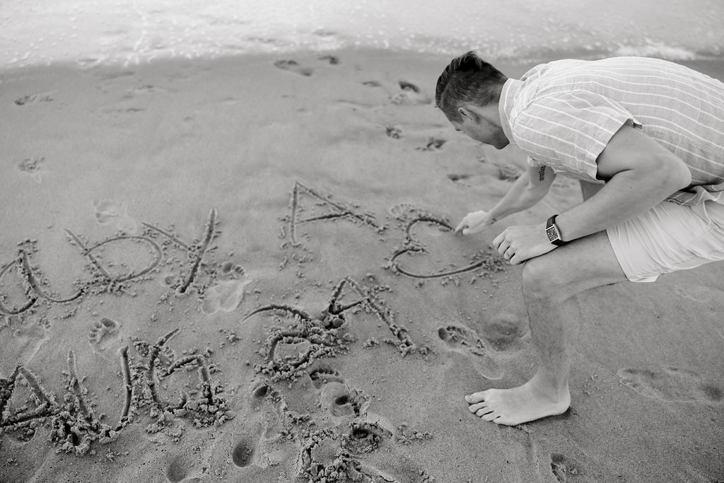 Destination Wedding Photographer captures man writing in sand to announce pregnancy