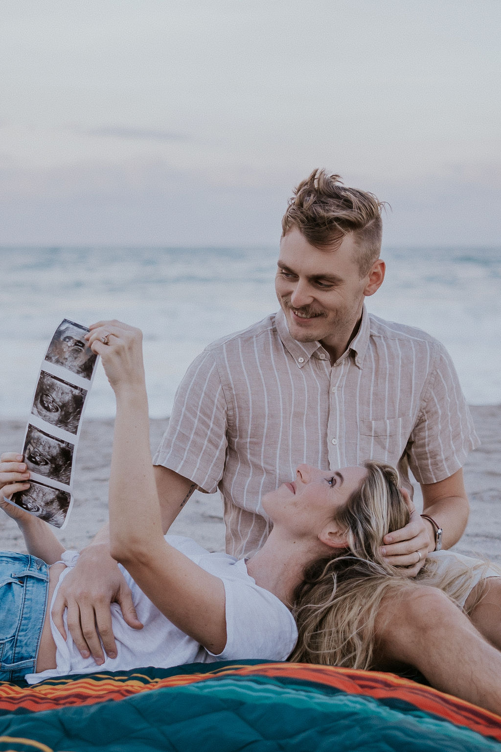 Destination Wedding Photographer captures couple sitting on blanket looking at ultrasound pictures