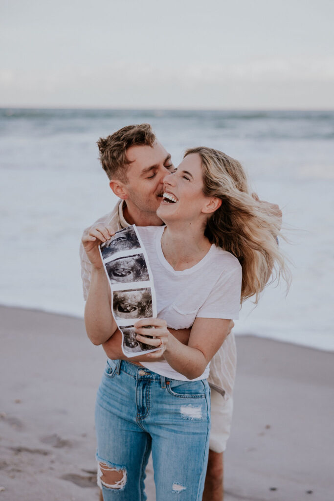 Destination Wedding Photographer captures man and woman laughing together while looking at ultrasounds