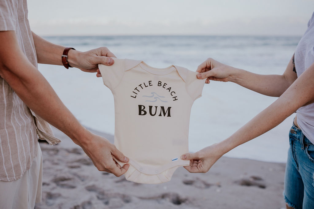 Destination Wedding Photographer captures couple holding onesie to announce pregnancy